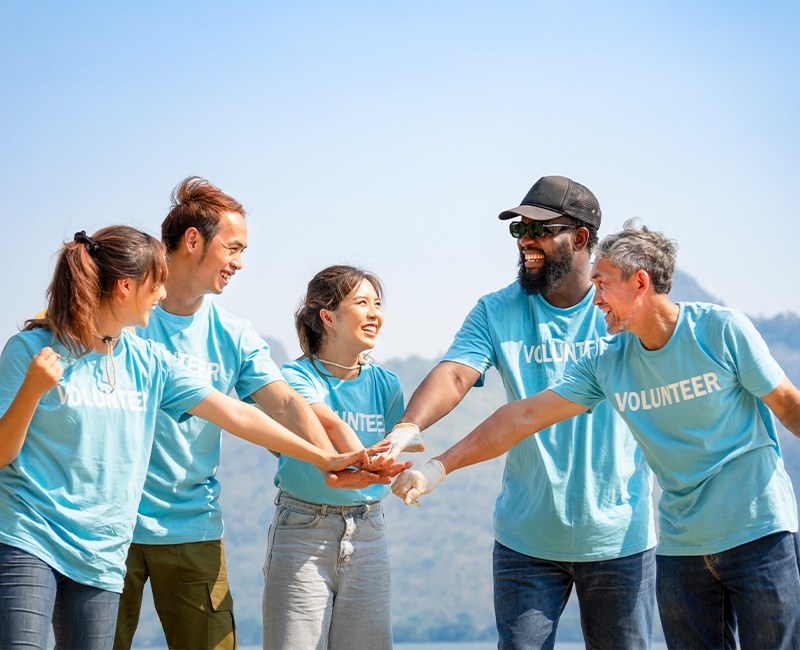 group of diverse ethnicity volunteers smiling,stacked hands together gesture of engage in some sort of teamwork activity while volunteering