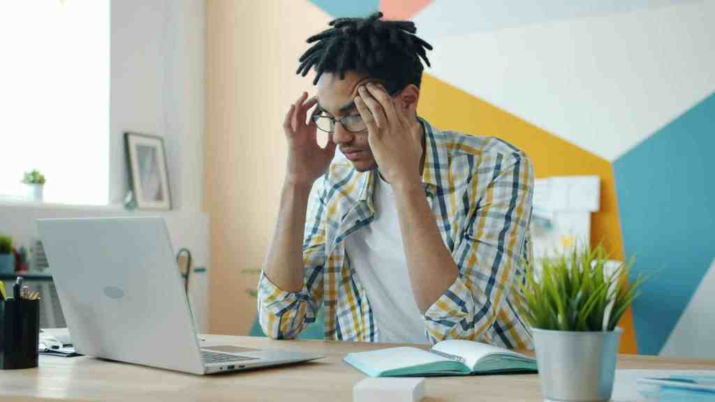 Man sitting at a laptop with his hands against his temples.